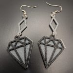 Black geometric diamond dangle earrings with silver diamond-shaped connectors and fish hook fastenings displayed on a dark background.