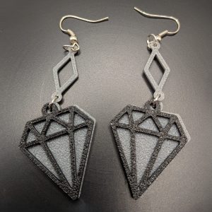 Black geometric diamond dangle earrings with silver diamond-shaped connectors and fish hook fastenings displayed on a dark background.