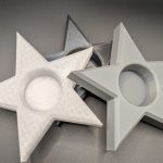 Large star-shaped tea light candle holders in silver, pearl white, and black displayed on a dark background.